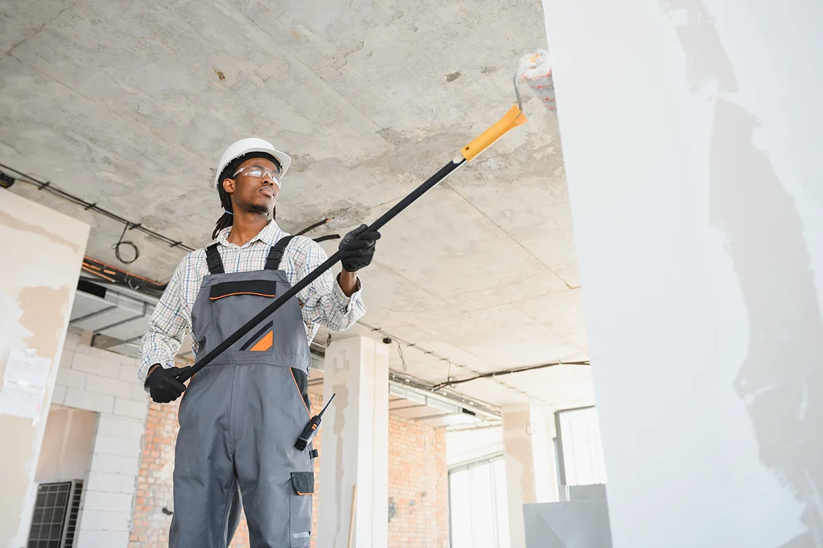 Construction Worker Painting Wall With Roller In Building Under Construction